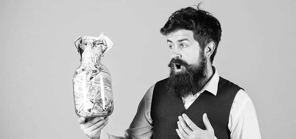 A bearded man gasping while looking at a jar full of money.