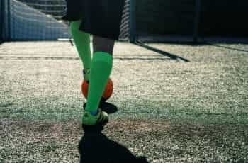 A footballer in green socks and boots, with foot on orange ball.