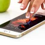 A smartphone lying down flat on a desk with a hand about to tap on its screen.