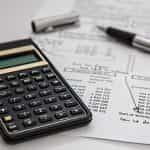 A calculator and fountain pen lying flat on a table on top of paperwork showing the financial performance of a company on it.