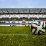 A football on a grass pitch in a stadium.