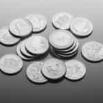 A collection of silver coins of different currencies lying on a table, some showing heads and other tails, with some stacked on top of one another while others lay around alone.