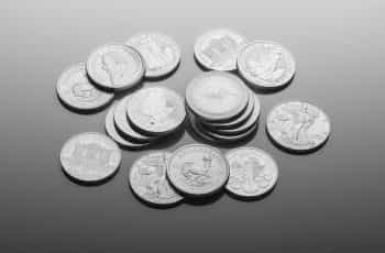 A collection of silver coins of different currencies lying on a table, some showing heads and other tails, with some stacked on top of one another while others lay around alone.