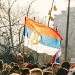 A crowd of people standing around a red, blue, and white flag.