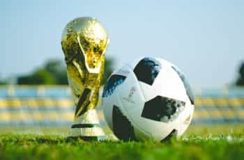 The golden World Cup trophy sits on a soccer field next to a soccer ball.