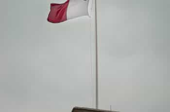 A red and white flag against a cloud sky.